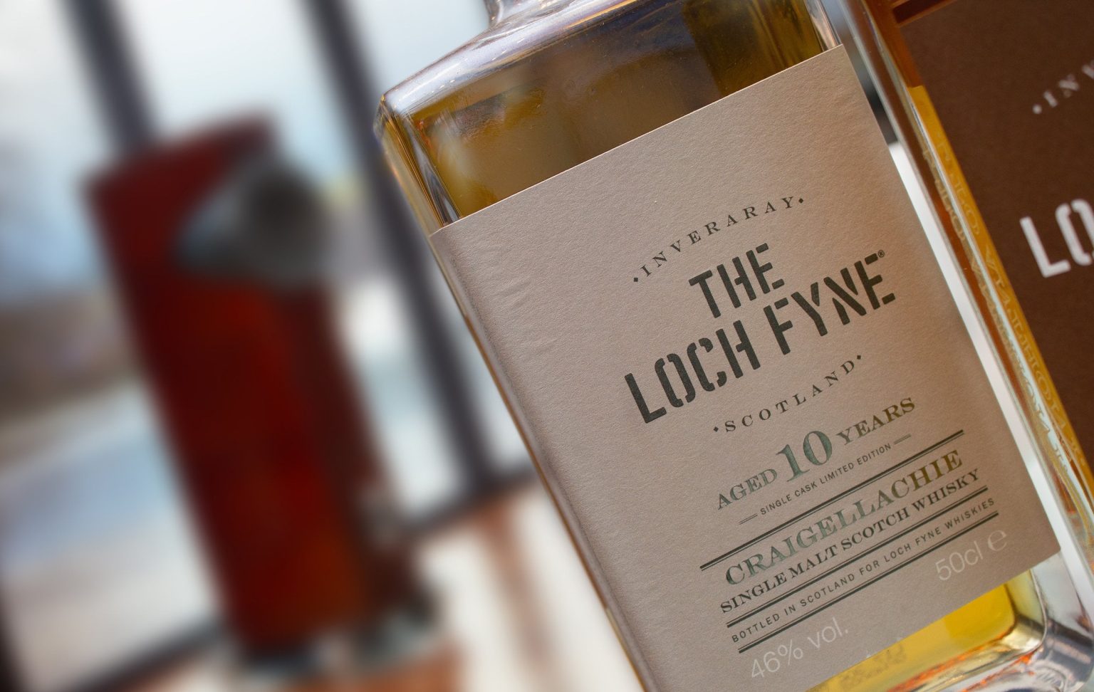 Botella de whisky Loch Fyne junto a un parlante Fyne Audio F1-10